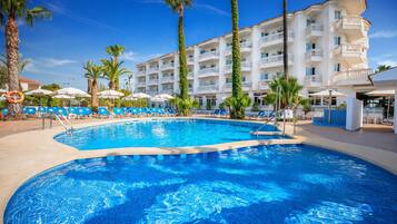 Una piscina con sillones de descanso, palmeras y un edificio de hotel de varios pisos.