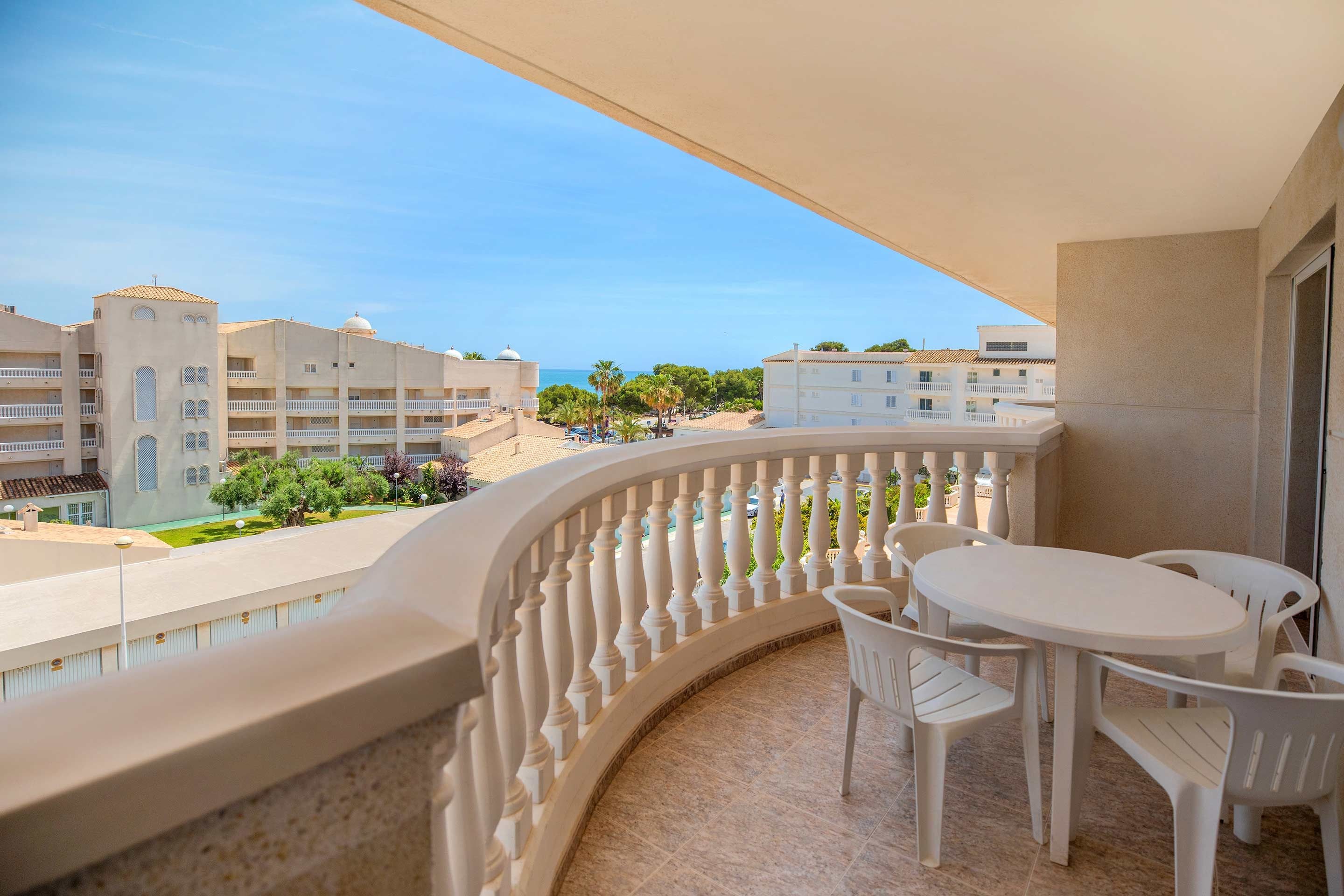 A balcony with a white table and chairs, a curved balustrade, and a view of buildings and palm trees.