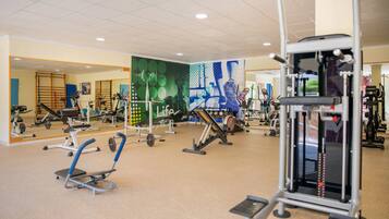 Un gimnasio con equipos de ejercicio variados, espejos y suelo de baldosas.