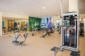 Ein Fitnessstudio mit verschiedenen Trainingsgeräten, Spiegeln und einem gefliesten Boden.