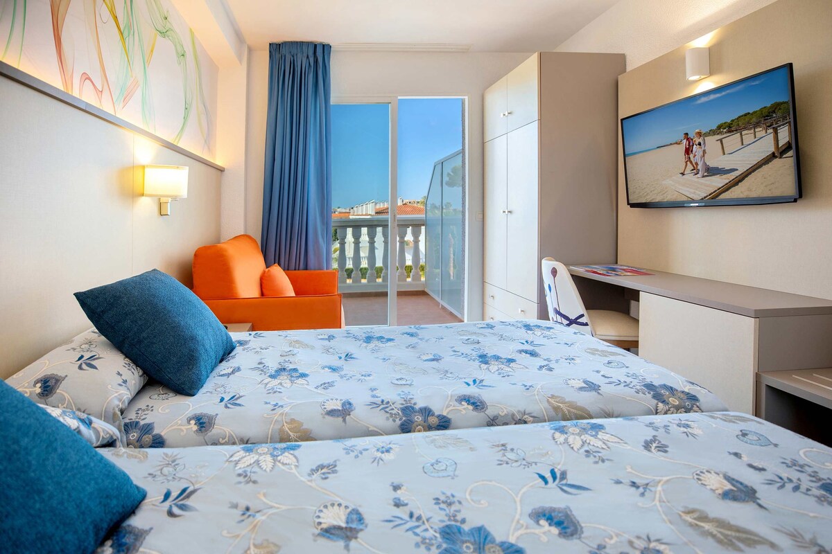 Ein Hotelzimmer mit Bett, Schreibtisch, Sessel, Fernseher und einem Balkon mit Blick.