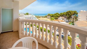 Een balkon met een witte balustrade, uitzicht op een strand en een zwembad.