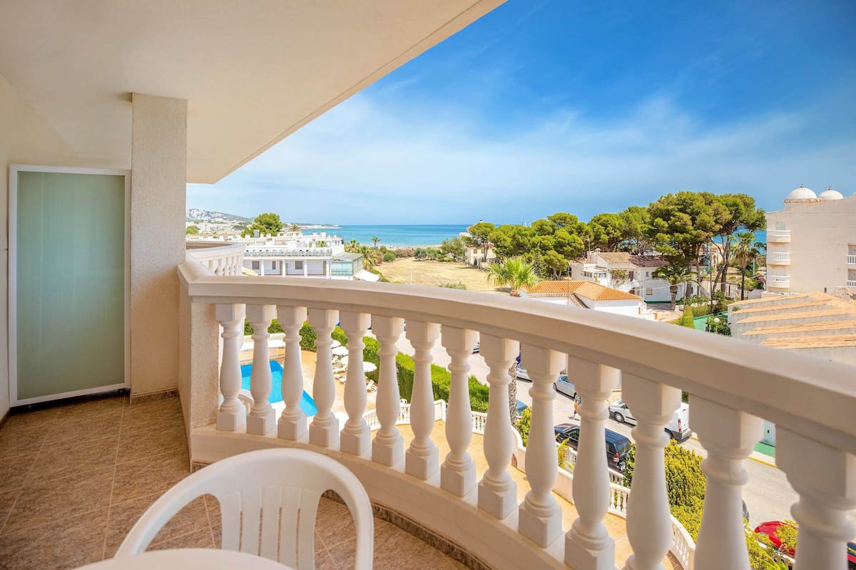Un balcon doté d’une balustrade blanche, avec vue sur une plage et une piscine.