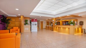 Een hotel receptie met een incheckbalie, een zithoek en een bord dat online inchecken promoot.
