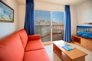 Une chambre d’hôtel moderne avec un canapé rouge, une table basse en bois, un téléviseur à écran plat et un balcon agrémenté de rideaux bleus.