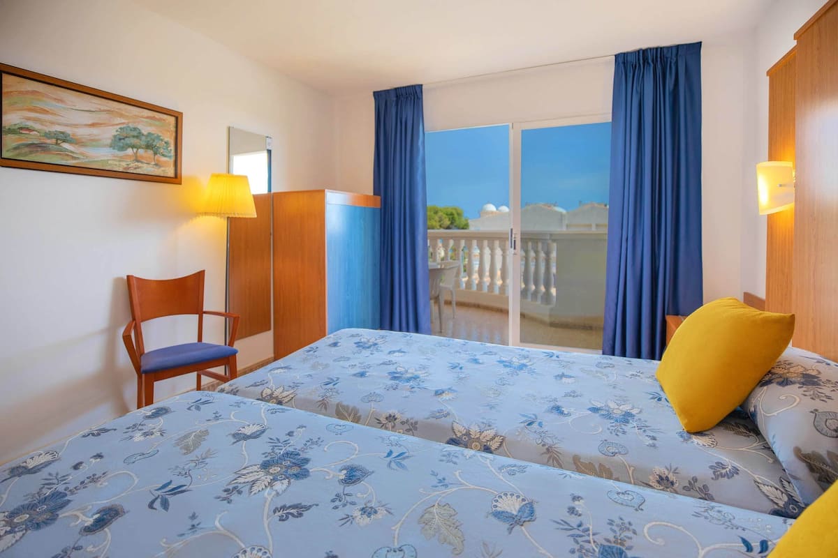 Une chambre d’hôtel avec un lit, une chaise, une lampe et un balcon avec des rideaux.