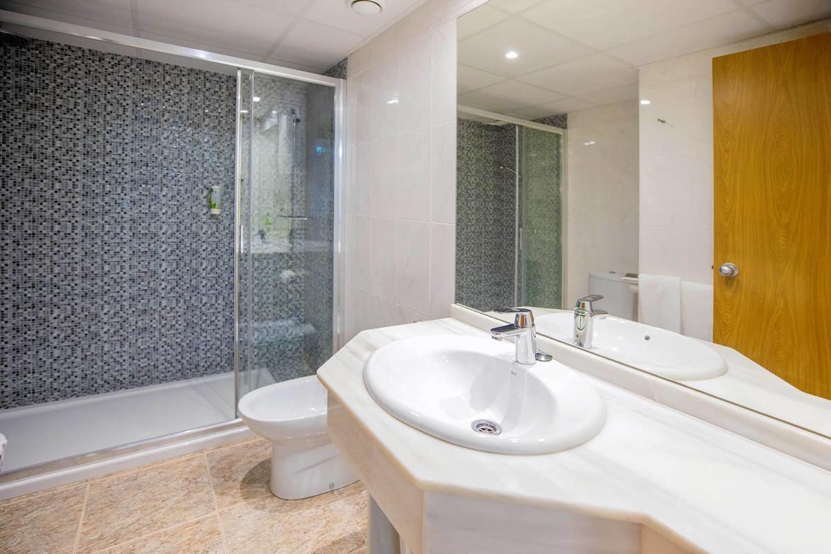 Une salle de bain moderne avec une douche à parois de verre, un lavabo blanc et une porte en bois.