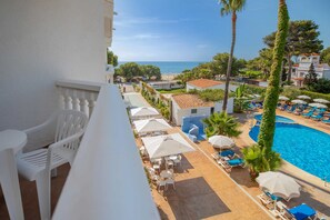 Un espace aménagé au bord de la piscine, avec des chaises longues et des parasols, une vue dégagée sur la mer et un bâtiment à la façade blanche.