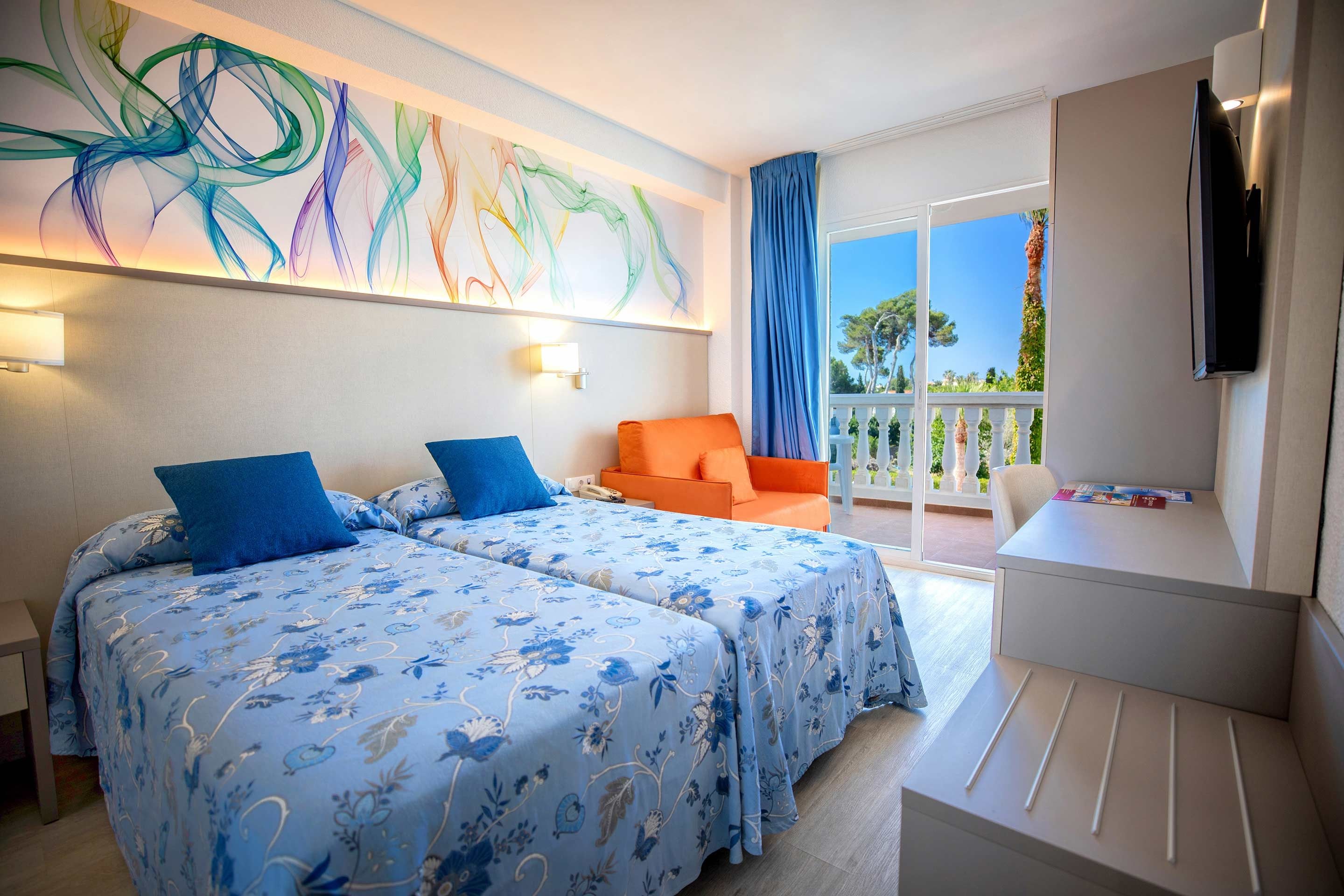 Habitación de hotel con dos camas, un escritorio, una silla, un televisor y un balcón con vistas.