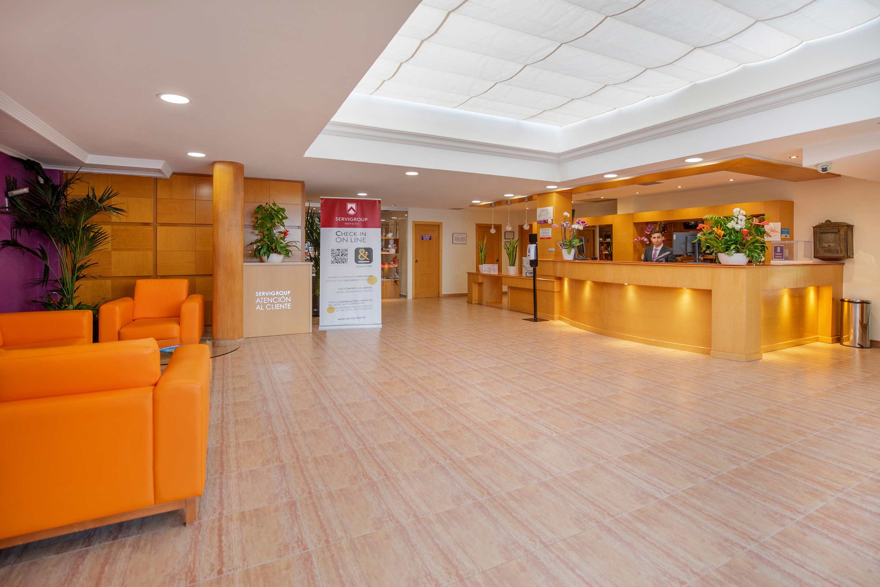 Zona de recepción de un hotel con mostrador de registro, área de descanso y un cartel que promociona el registro en línea.