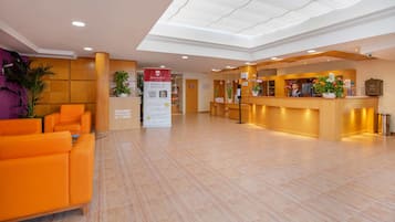 Zona de recepción de un hotel con mostrador de registro, área de descanso y un cartel que promociona el registro en línea.