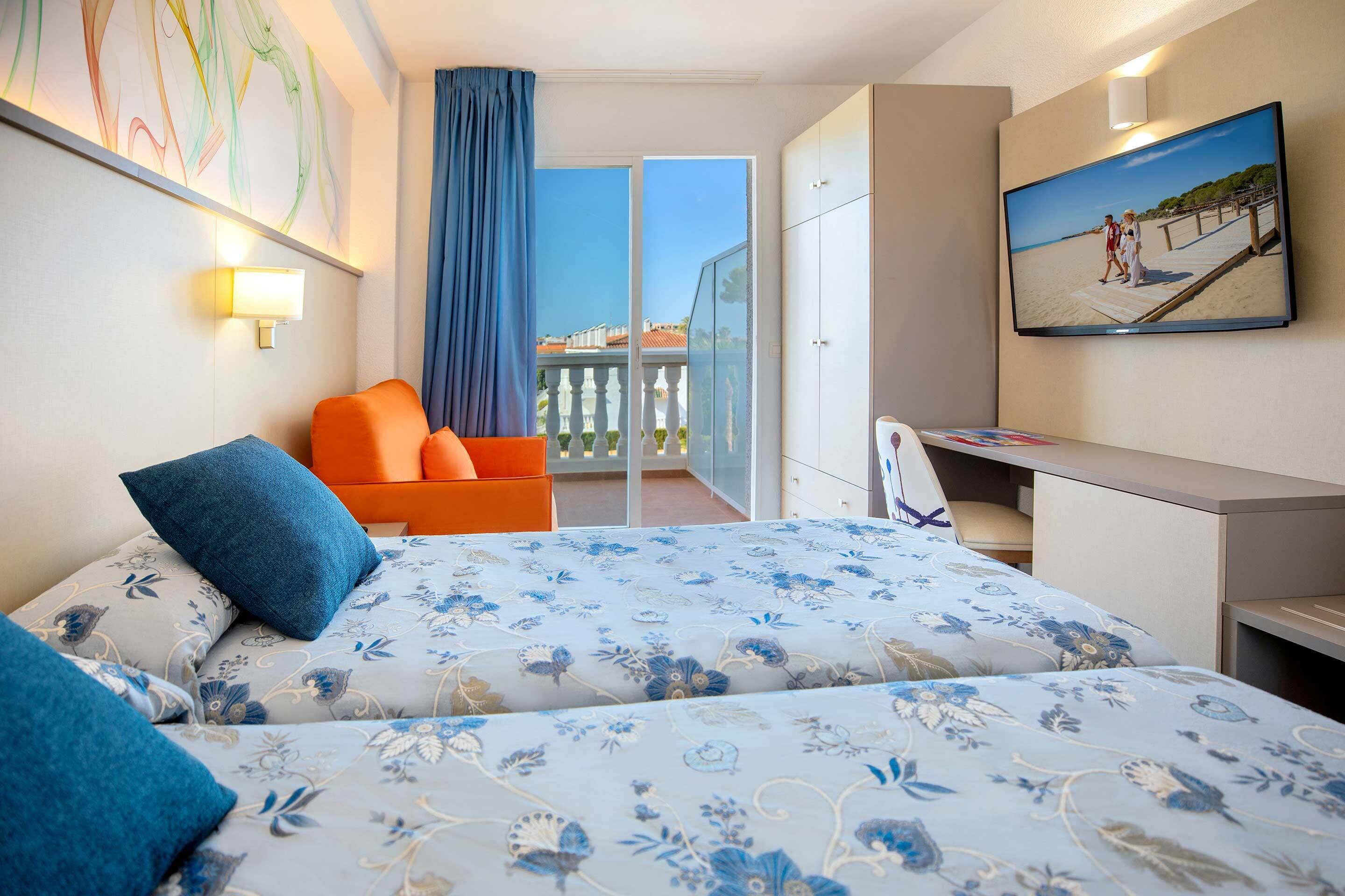 Habitación de hotel con cama, escritorio, silla, televisión y balcón con vistas.