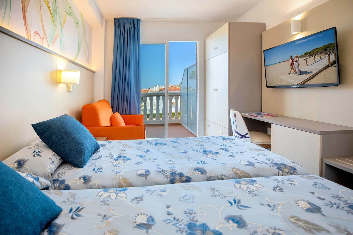Une chambre d’hôtel équipée d’un lit, d’un bureau, d’une chaise, d’une télévision et d’un balcon avec vue.