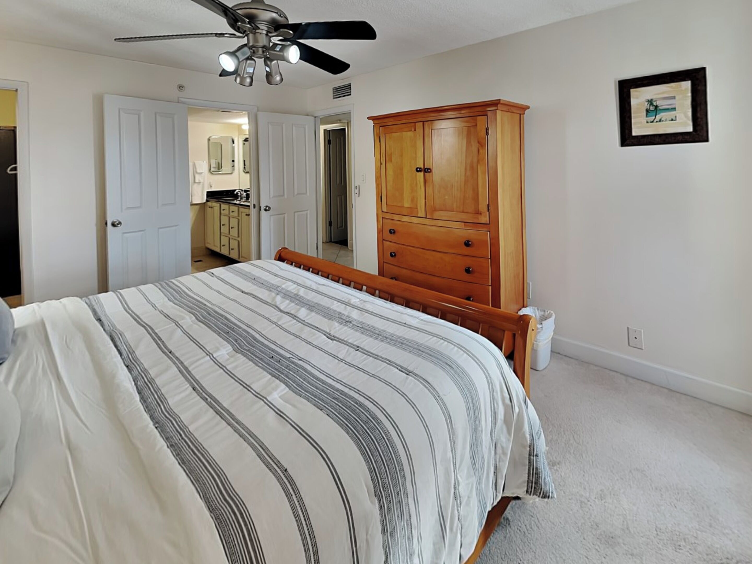 A bedroom with a bed, a wooden wardrobe, a ceiling fan, and a framed picture on the wall.