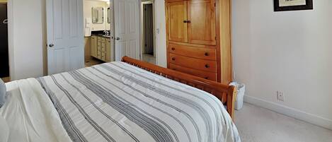 A bedroom with a bed, a wooden wardrobe, a ceiling fan, and a framed picture on the wall.