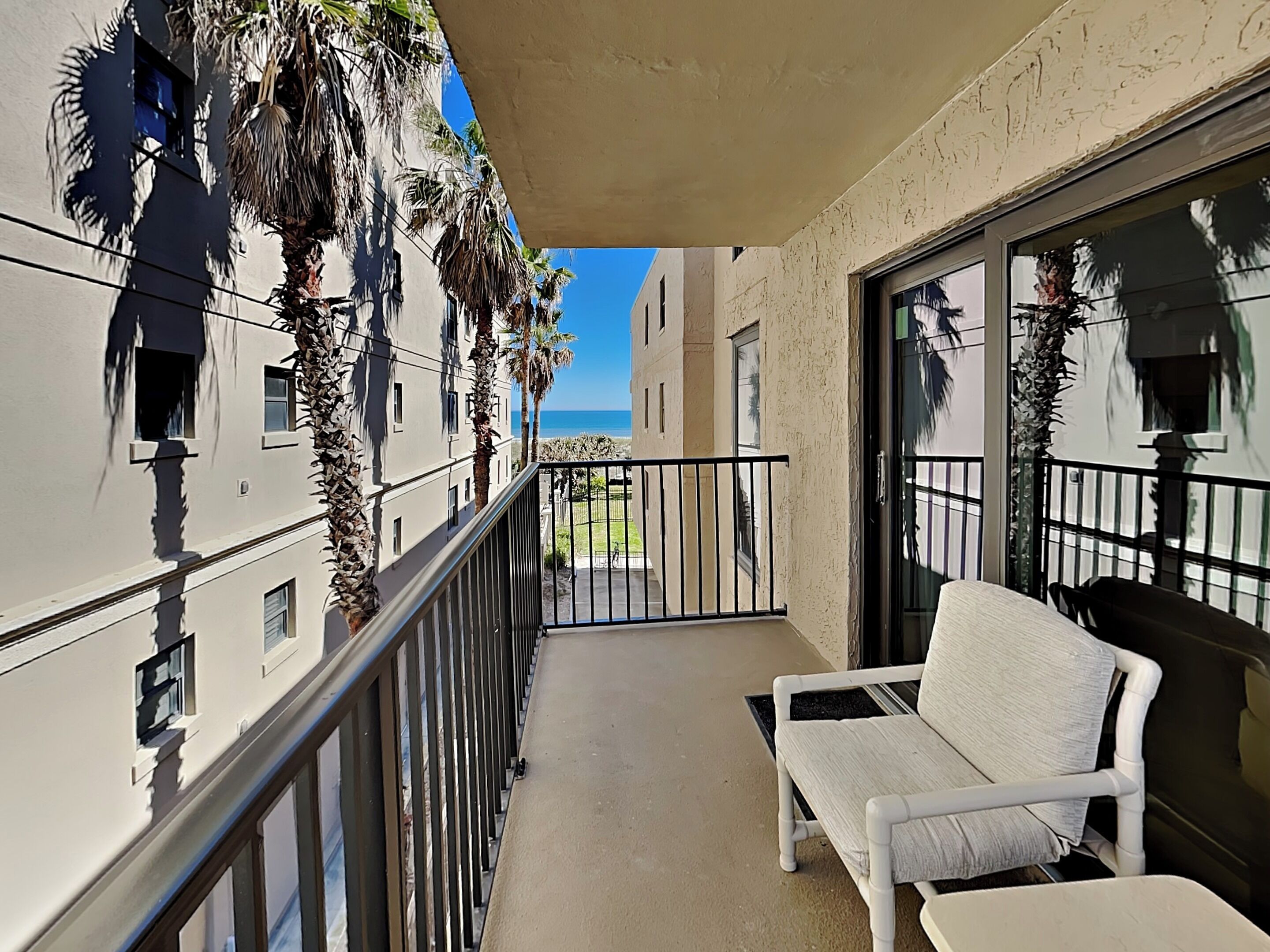 A balcony with a white chair, a metal railing, and a view of the ocean.