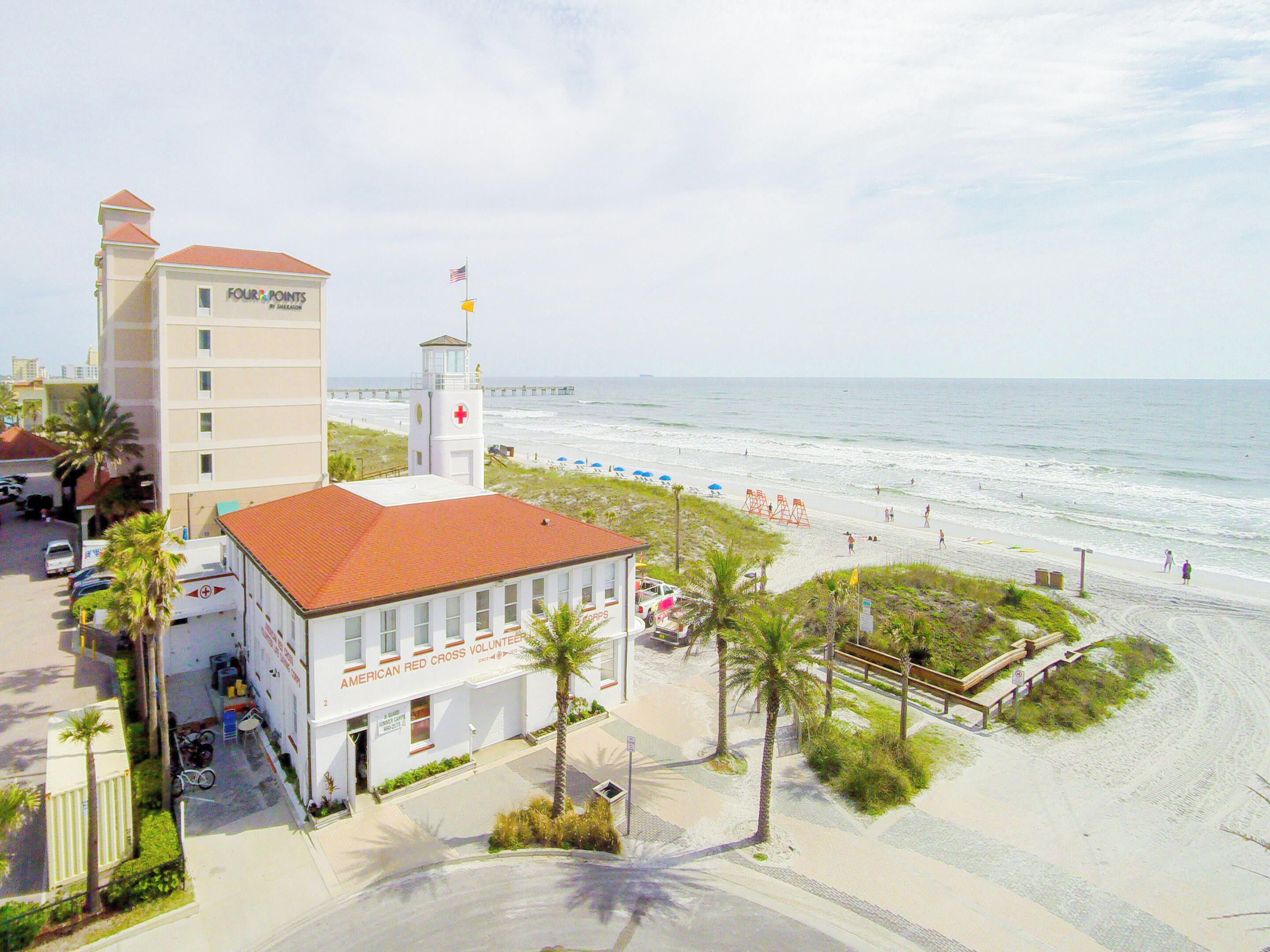 A coastal building with a red roof, a flag, and a beach in the background.