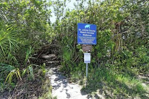 En skylt som visar vägen till strandpromenaden vid St. Johns County Beach, med en sköldpadds symbol, omgiven av tät vegetation.