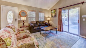 A living room with a sofa, a coffee table, a chandelier, a door with a stained glass window, and a sliding glass door leading to a patio.