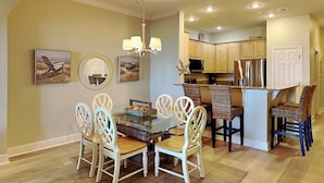 A dining area with a glass-top table, white chairs, and a chandelier. - Cinnamon Beach 4 by Distinctive Beach Rentals (Palm Coast)