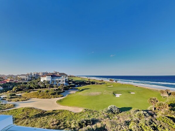 Een golfbaan aan de kust met een clubhuis, uitzicht op de oceaan en een heldere lucht.