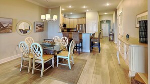 A spacious kitchen with wooden cabinets, a dining area with a glass table, and a hallway leading to a bedroom. - Cinnamon Beach 4 by Distinctive Beach Rentals (Palm Coast)