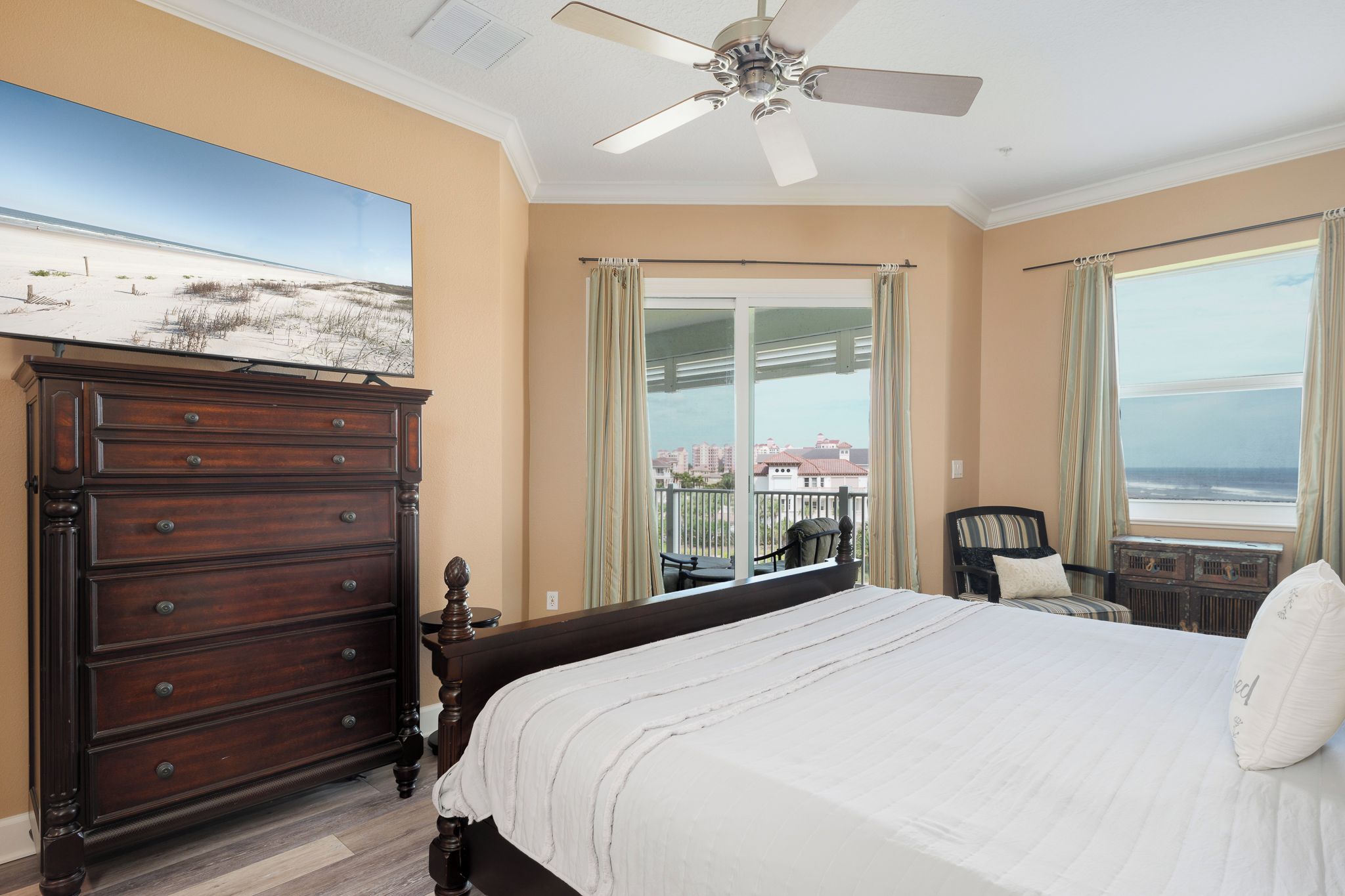 Une chambre dotée d’un grand lit, d’une commode, d’un ventilateur de plafond et d’un balcon offrant une vue sur l’océan.