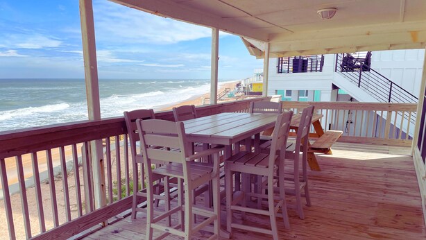 A wooden deck with a table and chairs, overlooking a beach and ocean.