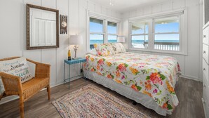 A bedroom with a bed, a chair, a nightstand, a ceiling fan, and a view of the ocean.