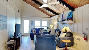 A living room with a blue sofa, a round table, a television, and a ceiling fan.