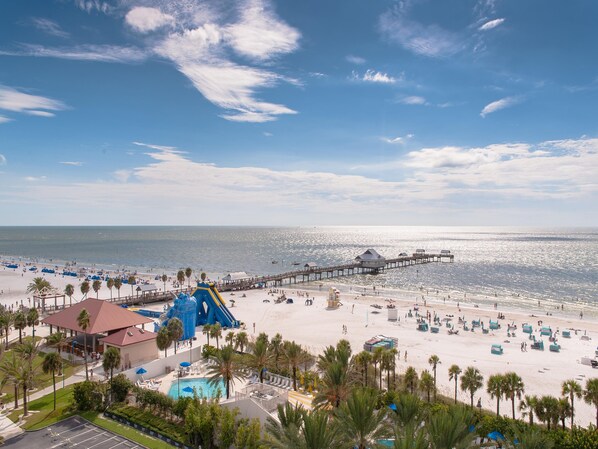 A beach resort with a large pool, beach umbrellas, and a pier extending into the ocean.