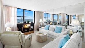 A spacious living room with a large window, a flat-screen TV, and a comfortable seating area. - Casa Del Mar G-608 by Distinctive Beach Rentals (St. Petersburg)