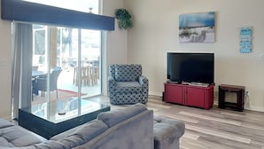 Ein Wohnzimmer mit einer Couch, einem gemusterten Sessel, einem Fernseher und einem Deckenventilator.