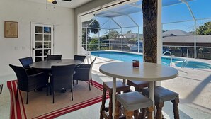 Ein Zimmer mit Blick auf einen Pool, einem runden Tisch und Korbstühlen.