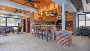 Ein großzügiger Patio-Bereich mit Kamin aus Backsteinen, hölzernen Barhocker und Grill.