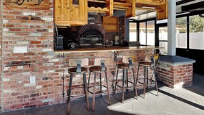 A brick wall with a wooden bar and stools, a brick oven, and wooden cabinets. - Beach Daze by Distinctive Beach Rentals (Palm Coast)