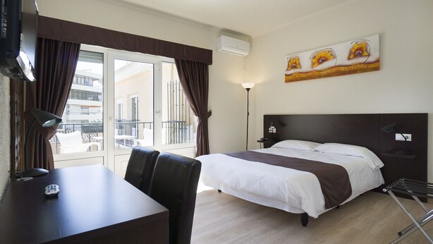 Una habitación de hotel con cama, escritorio, silla, lámpara y un cuadro en la pared.