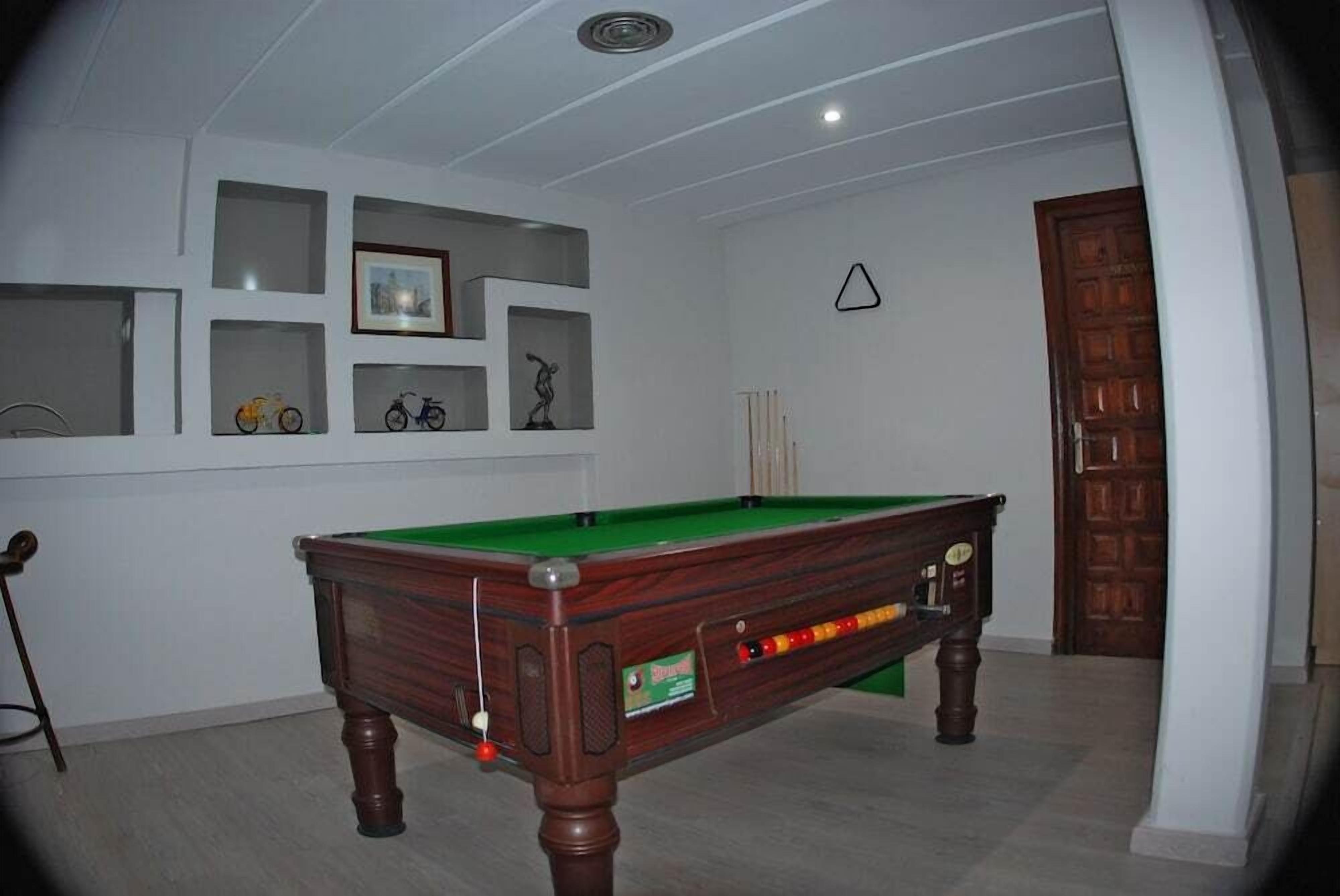 Une table de billard dans une pièce aux murs blancs, avec des étagères ornées de tableaux encadrés et une porte en bois.