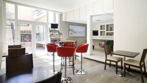 Un interior moderno con una zona de bar, sillas rojas, una mesa de billar y vistas al exterior.