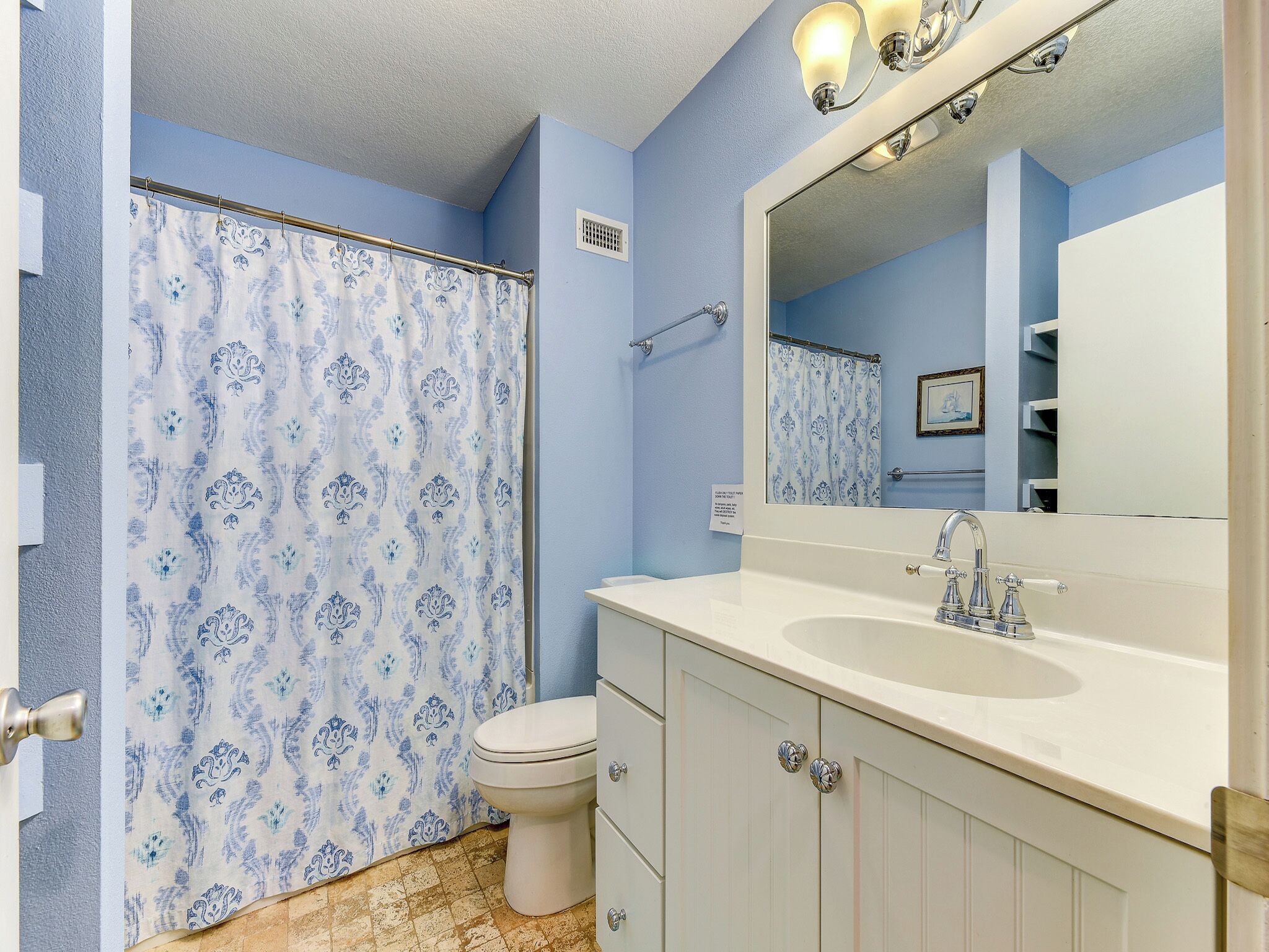 A bathroom with a shower curtain, toilet, sink, and cabinets.