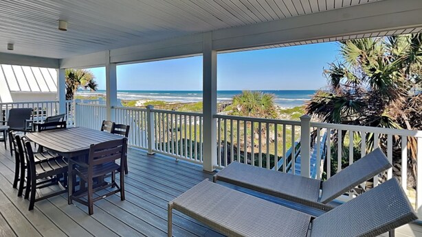 A covered outdoor area with a table and chairs, a lounge chair, and a view of the beach and ocean. - Four Palms by Distinctive Beach Rentals (St. Augustine)