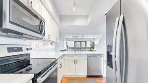 A modern kitchen with white cabinets, stainless steel appliances, and a wooden floor. - Island House by Distinctive Beach Rentals (St. Augustine)
