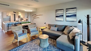 A modern living room with a grey sofa, wicker chairs, a coffee table, and a blue patterned rug. - Island House by Distinctive Beach Rentals (St. Augustine)