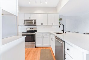 A modern kitchen with white cabinets, stainless steel appliances, and a wooden floor. - Island House by Distinctive Beach Rentals (St. Augustine)