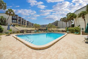 A rectangular swimming pool with a tiled deck, surrounded by palm trees and lounge chairs. - Island House by Distinctive Beach Rentals (St. Augustine)