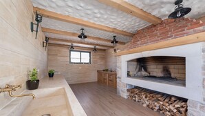 A modern kitchen with a large sink, wooden beams, a brick fireplace, and a window.