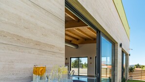 An outdoor seating area with a table set for drinks, a glass tray, and a clear view of the building's interior and surrounding greenery.