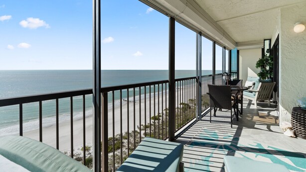 A balcony with a view of the ocean, furnished with chairs and a table, and a potted plant. - Ocean Sands 908 by Distinctive Beach Rentals (Madeira Beach)