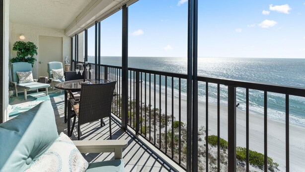 Ein Balkon mit Blick auf das Meer, ausgestattet mit einem Tisch, Stühlen und einer Couch.