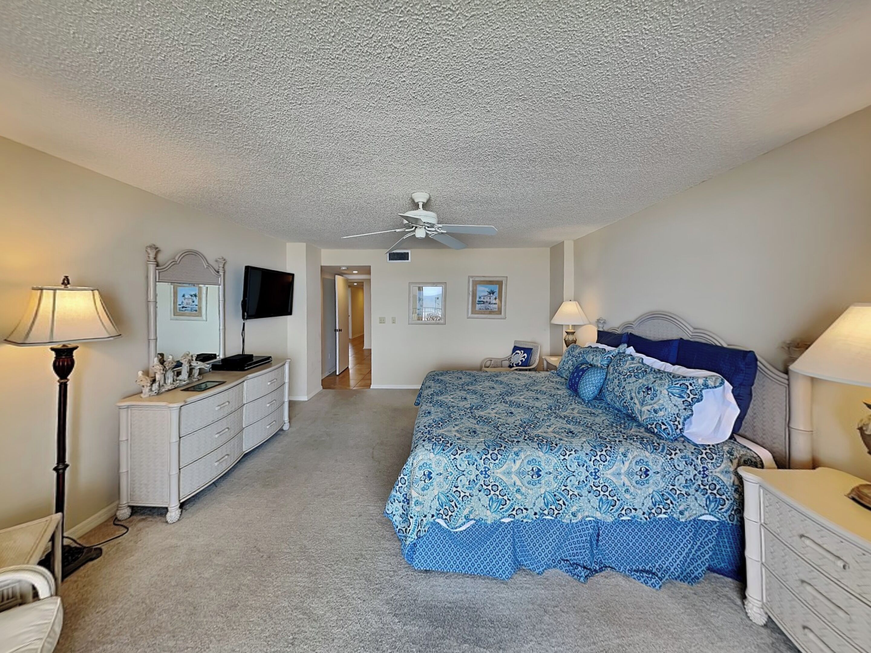 A bedroom with a bed, dresser, lamp, and ceiling fan.